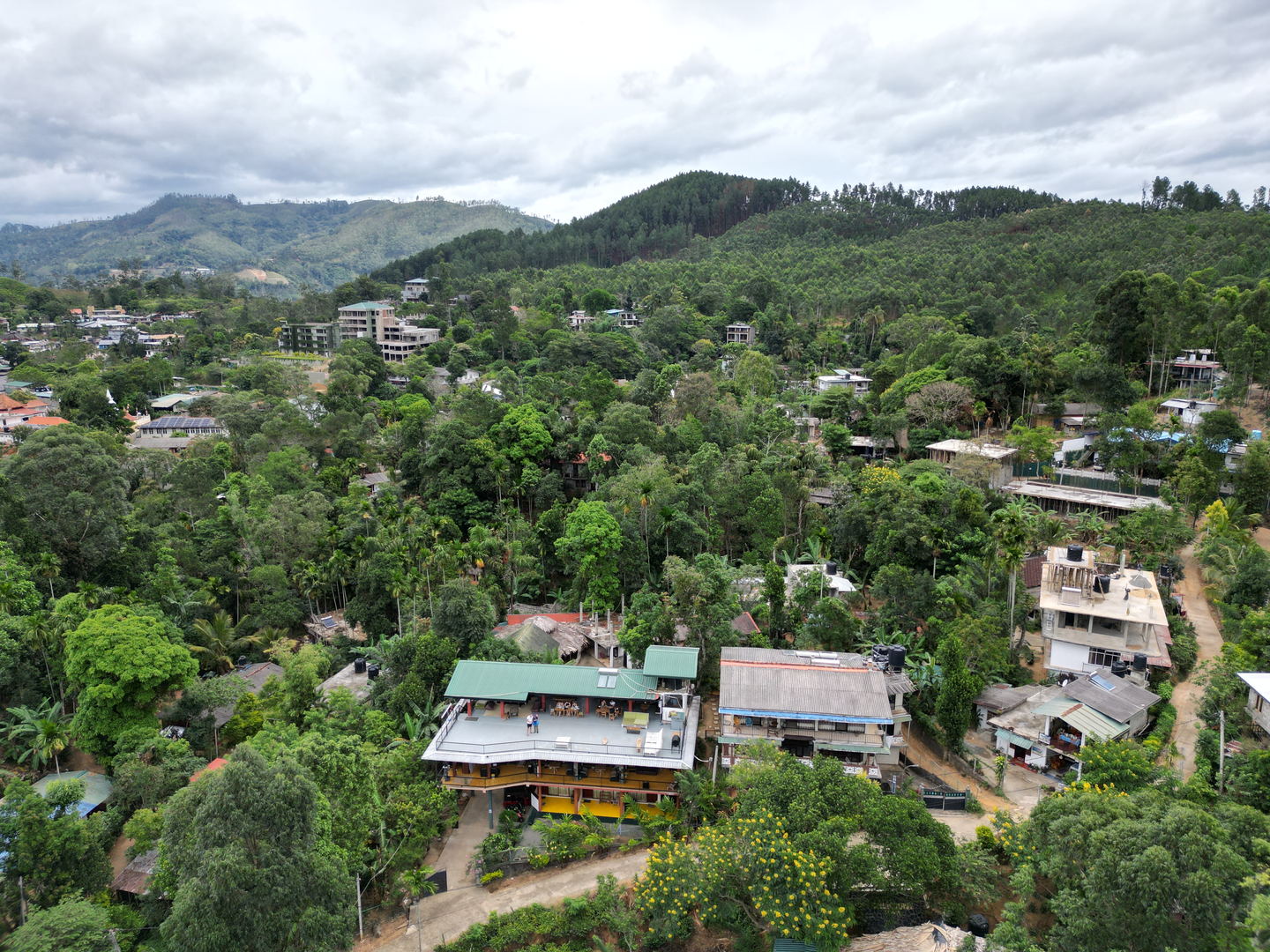 The hillside above Ella from the air: houses with green and red roofs scattered among trees, and wooded hills behind. The town, not us.