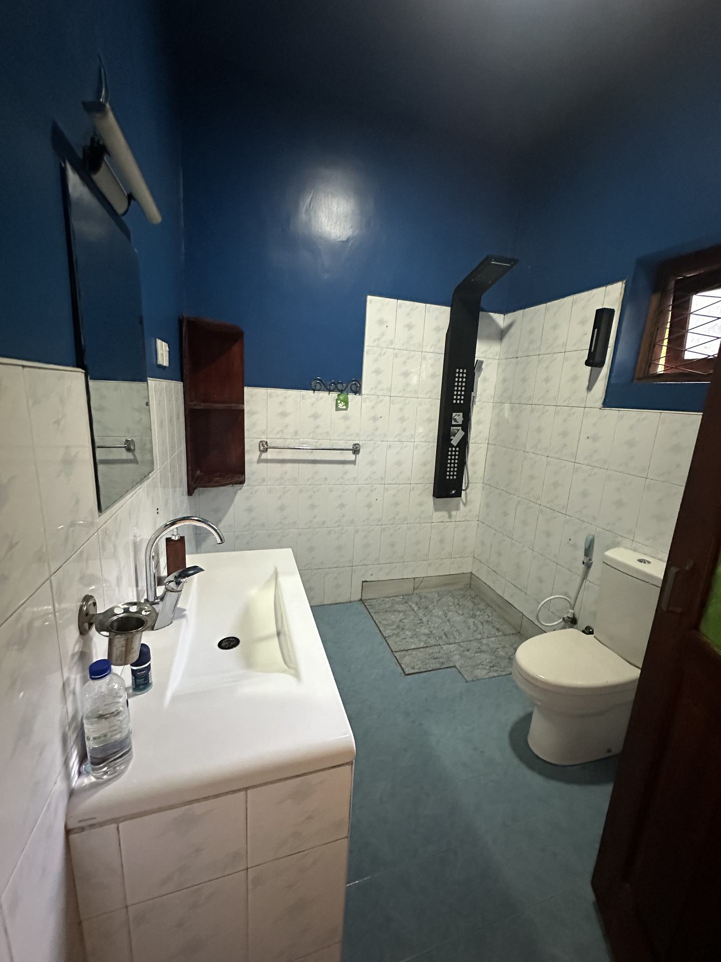 A wet room painted deep blue above white tile, with a black rain-shower panel, a wide basin and a toilet.