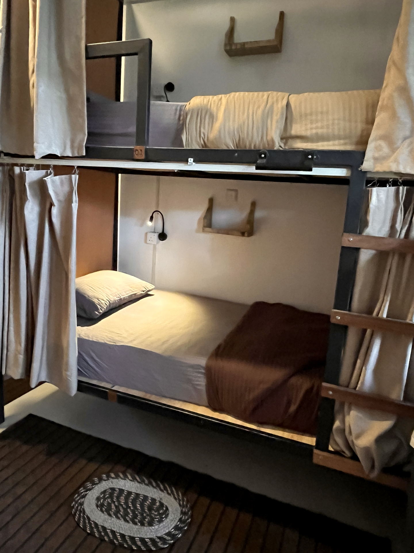 A lower bunk with a folded towel on the mattress, a timber shelf at the head end and a hook on the frame.
