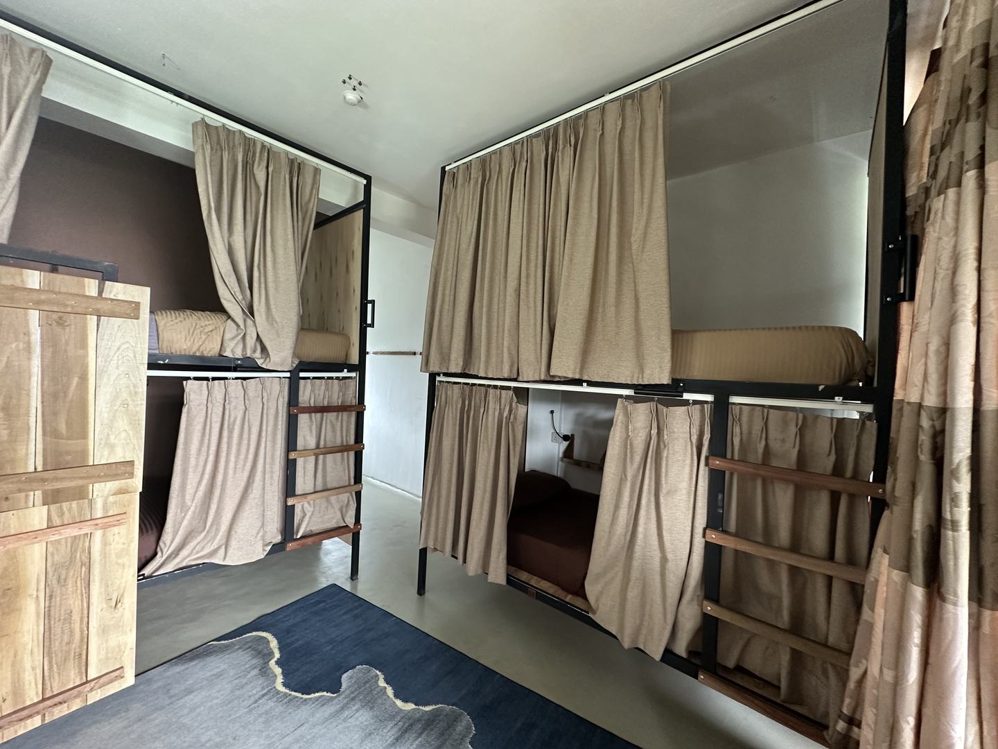 A four-bed dormitory: two sets of bunks with full-length curtains, a timber wardrobe and a rug between them.