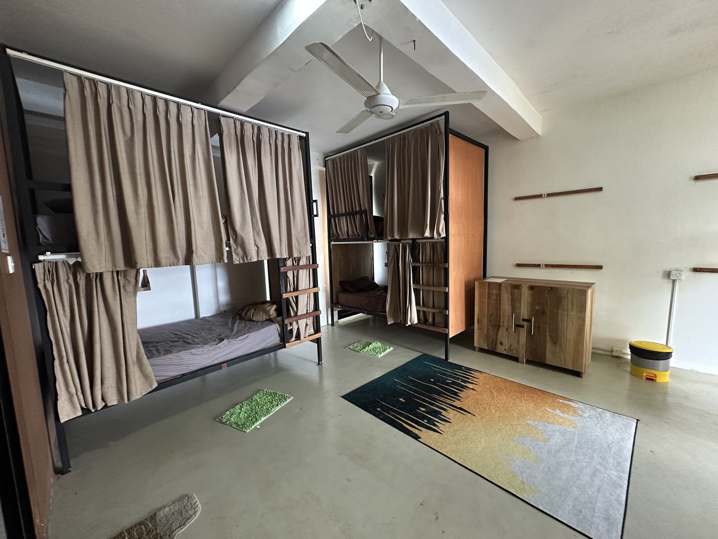 The six-bed dorm: two sets of curtained bunks, a ceiling fan, a timber wardrobe and rugs on a bare floor.