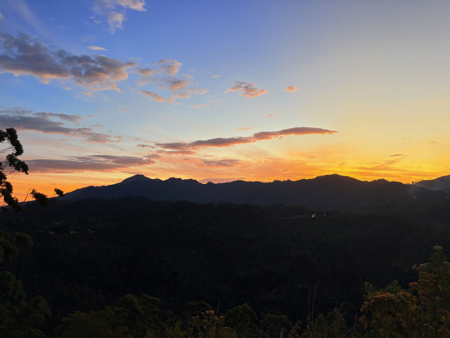 Sunrise behind layered hill silhouettes, the sky orange above and the valley still dark.