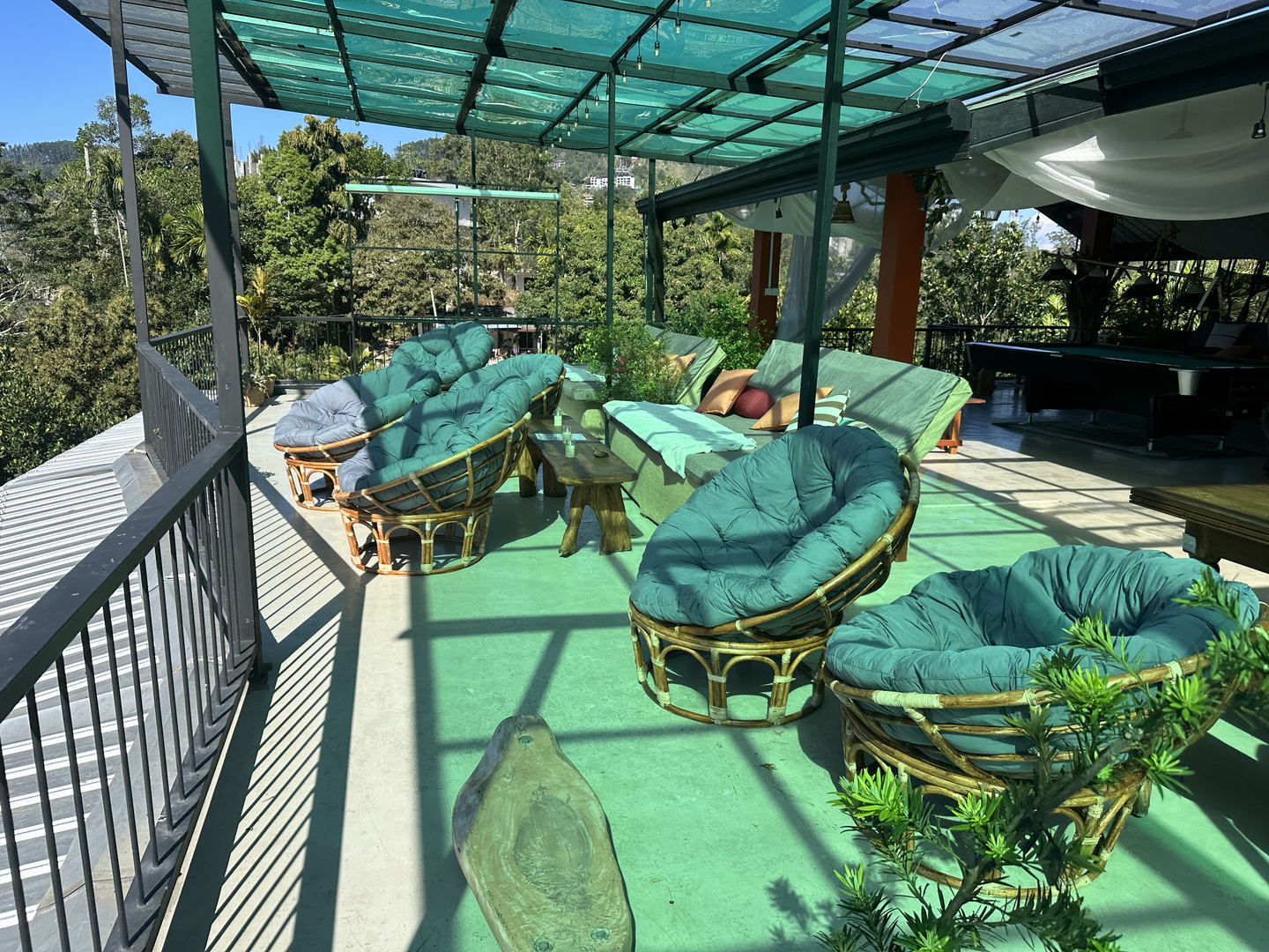 Round rattan chairs with thick cushions and a long bench along the open side of the terrace, with the pool table beyond.
