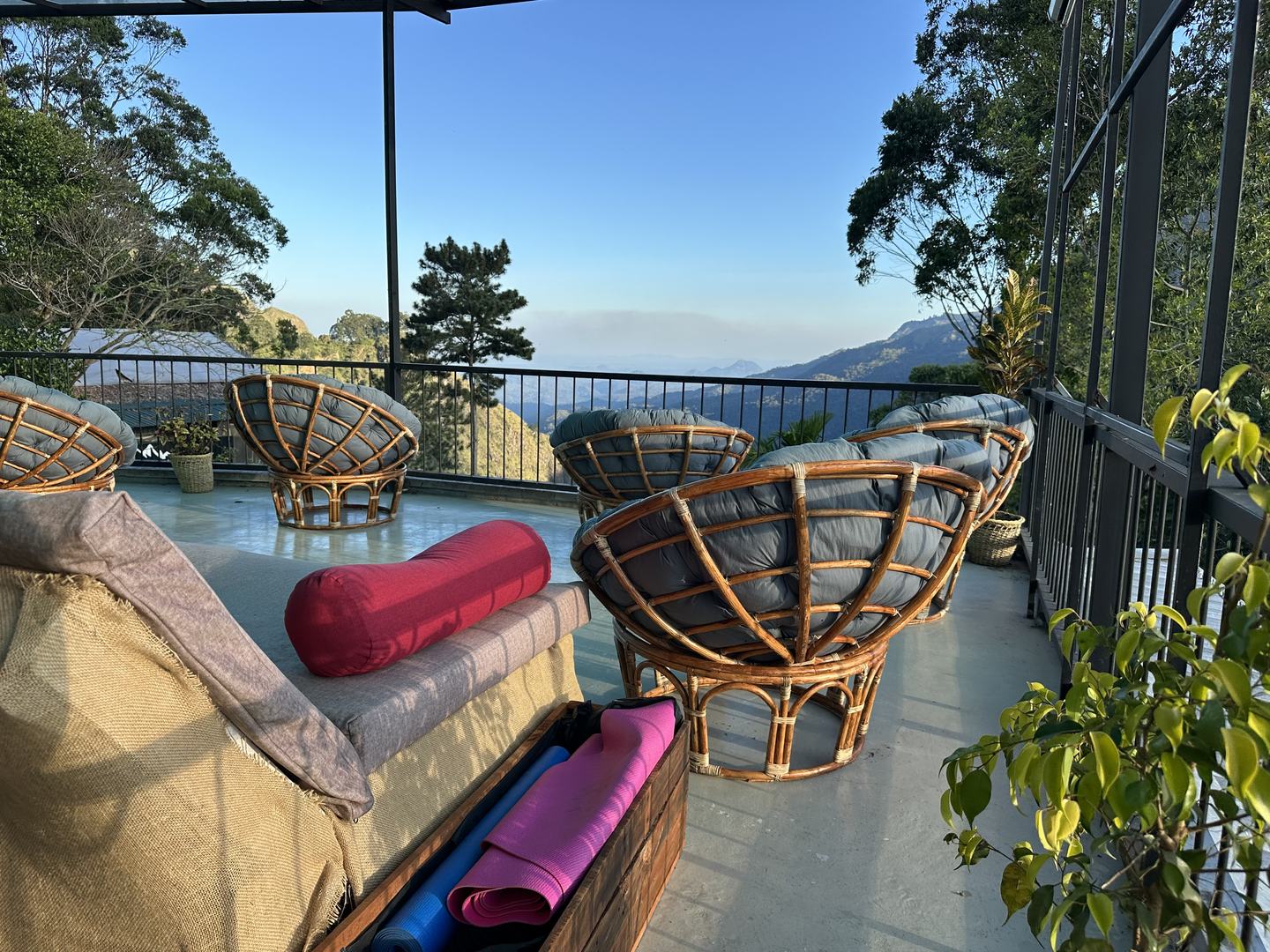 Round rattan chairs on the terrace facing the valley, with rolled yoga mats stored in a timber crate in the foreground.